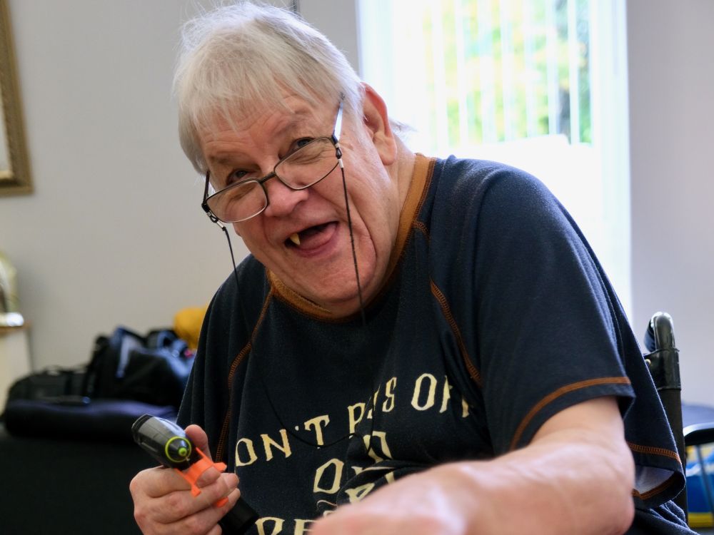 A man in a dark t-shirt holding a hot glue gun and smiling