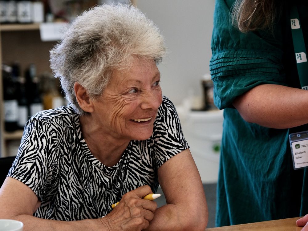 A silver haired lady smiles at a nearby person