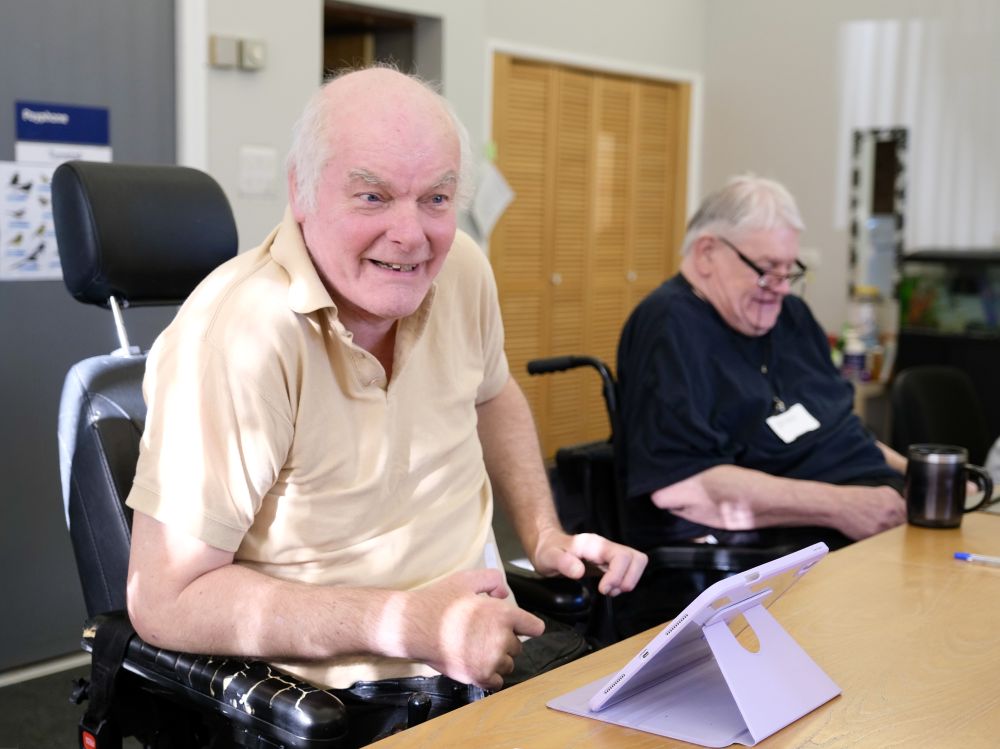 A man in a yellow polo has a cheeky grin while sitting in a wheelchair