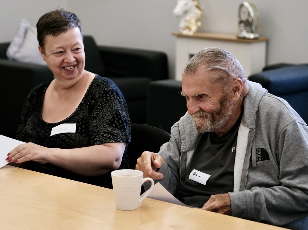A man and a woman sat at a table having a laugh. This image links to Robert's artwork page